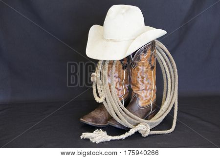Western boots, hat and rope against a black background