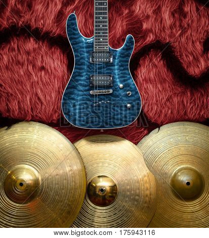 Blue electric guitar with three cymbals on faux fur wall. Musical instruments background