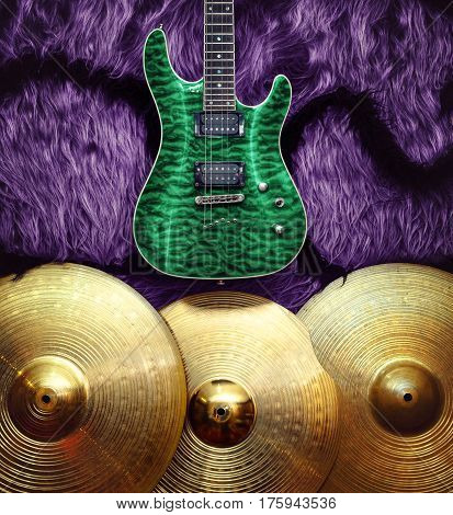 Green electric guitar with three cymbals on purple faux fur wall. Musical instruments background