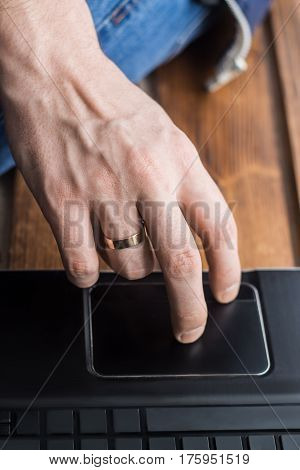 Close-up shot of men's hand touching trackpad on laptop. Empty space on keys. Wooden backdround