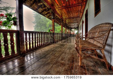 A pale teak wood garden bench on a stone terrace before a background of fall foliage.