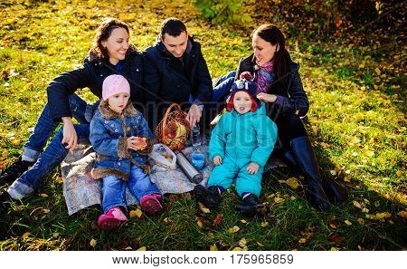 Happy Young Family Of Four Having Picnic At Meadow At Summer Day