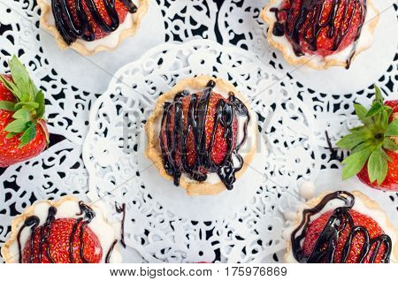 Strawberry cake with vanilla cream on white rusric wooden background. Sweet basket tartlet with strawberries and chocolate. Tasty summer dessert. Top view.