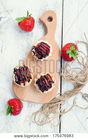 Strawberry cake with vanilla cream on white rusric wooden background. Sweet basket tartlet with strawberries and chocolate. Tasty summer dessert. Top view.