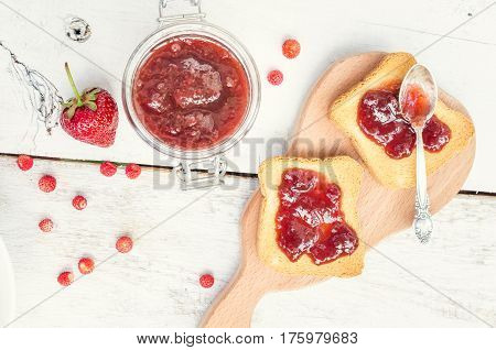Toasts with strawberry jam for breakfast on white rusric wooden background. Top view.