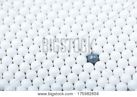Black Bulb Among Many White Ones. Background Of Airsoft Balls