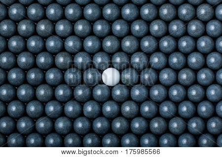 White Airsoft Ball Is Among Many Black Balls. Background Of 6Mm Bbs