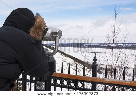 Man looking through a coin operated binocular at the St Laurent river during winter Quebec, Canada