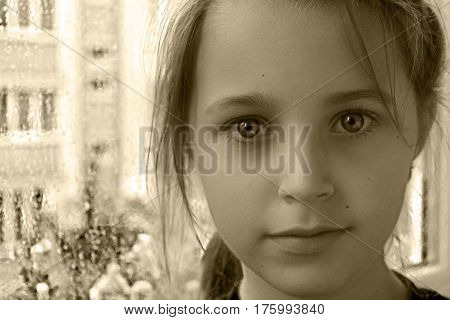 The girl looks into the camera. In the background window in rain drops.