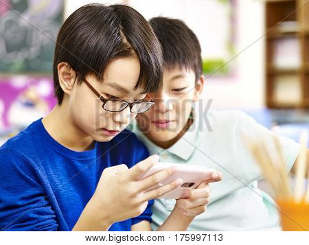 two asian primary school students playing online game using mobile phone.