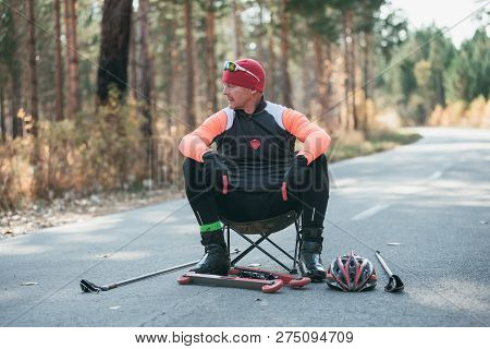 Training An Athlete On The Roller Skaters. Biathlon Ride On The Roller Skis With Ski Poles, In The H