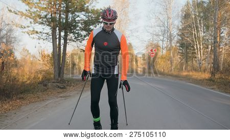 Training An Athlete On The Roller Skaters. Biathlon Ride On The Roller Skis With Ski Poles, In The H