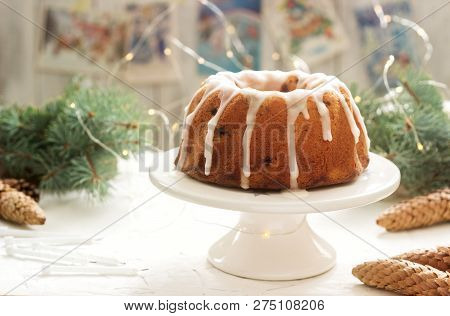 Pie With Raisins And Icing From Powdered Sugar On The Background Of Fir Branches And Garlands. Rusti