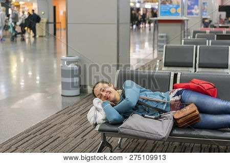 Young Woman Sleeping At The Airport While Waiting For Her Flight. Tired Female Traveler Sleeping On 