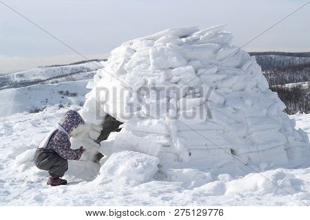 The Child Holds A Snowball Squatting At The Entrance To The Home Of Eskimos - Igloo