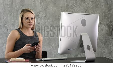 Young Smiling Business Woman Using Smartphone Near Computer In Office.