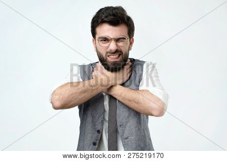 Man Grabs His Throat With Both Hands And Squints Intensely From The Pain In His Throat.