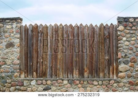 The Fence Of Logs And Stones Against The Blue Sky. Concept Of Captivity And Slavery.