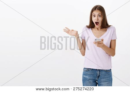 Amazed Attractive Sociable Young Female Student With Long Brown Hair Holding Smartphone Waving Raise