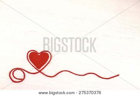 Single Red Felt Heart With Wool Red Yarn Making In The Shape Of Heart Around On White Wooden Backgro