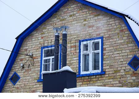 Two Black Metal Chimney Pipes On The Roof Under The Snow At The Front Of A Brick Wall With Windows