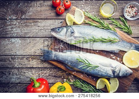 Fresh Raw Seabass And Ingredients For Cooking. Two Fish Seabass With Lemon, Spices And Herbs On Wood