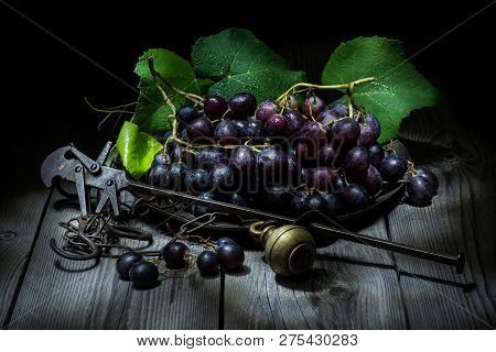 Still Life With Black Grapes In An Old Steelyard On Rough Wooden Table