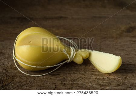 Head And Slice Of Typical Italian Caciocavallo Cheese On A Wooden Surface.