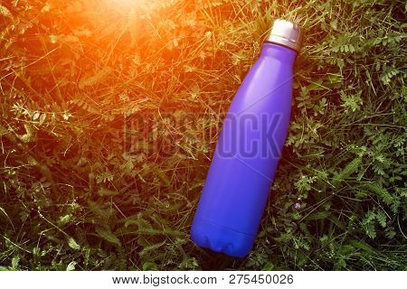 Stainless Thermos Water Bottle, Matte Blue Color. Mockup Isolated On Green Grass Background With Sun