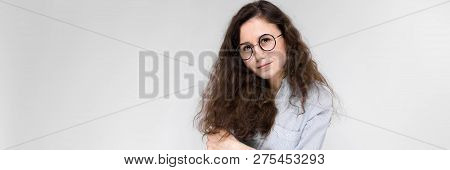 Portrait Of A Young Girl In Glasses. Beautiful Young Girl On A Gray Background. The Girl Is Holding 