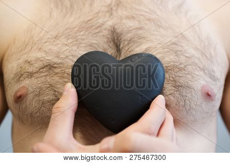 Close-up Of Black Stone Heart In Man Hands, On Body Torso Background.