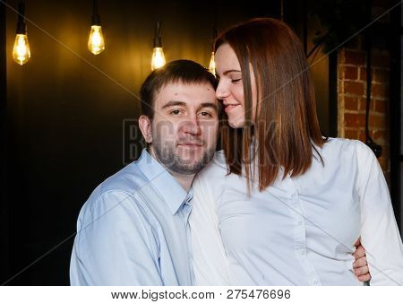 Young Red-haired Girl Sniffs A Mans Hair With Her Eyes Closed. Happy Young Couple In Lotf Interior A