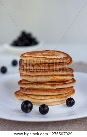 Stack Of American Pancakes And Fresh Blackcurrant Are Lying On A White Plate.