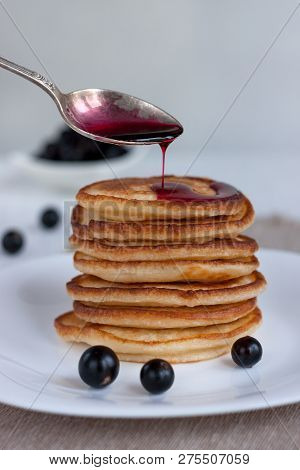 Stack Of American Pancakes With Blackcurrant Jam And Fresh Blackcurrant Are Lying On A White Plate.