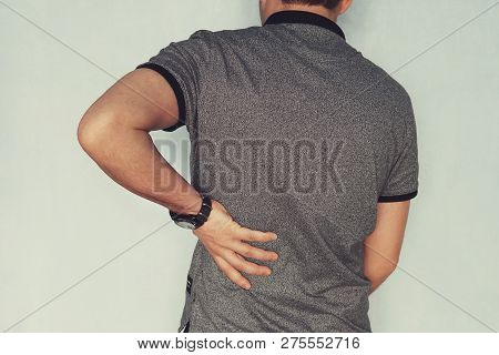 Image Of Man Suffering Back Pain Against Blue Background, Renal Failure. Patient Holds His Hand Behi