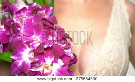 Close-up. Female Breast Closeup With A Large Bouquet Of Orchids In Their Hands. Female Breast Health