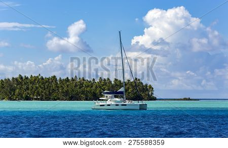 Lonely Catamaran In The Turquoise Lagoon On The Background Of The Island Of Tahaa In The Leeward Gro