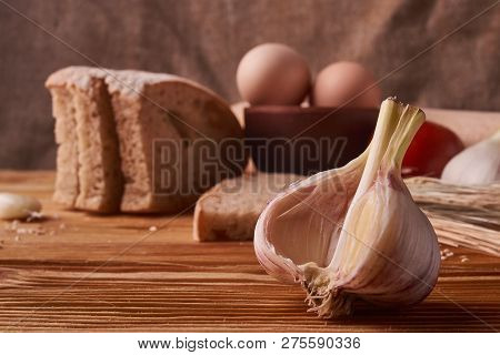 Garlic On A Wooden Table With Eggs In Clay Bowl, Tomato, Battledore And Wheat Sprouts