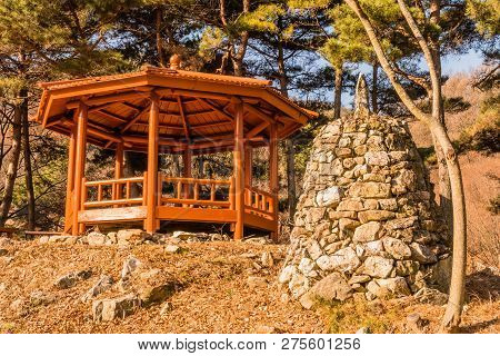 Stone Pyramid Next To Wooden Gazebo On Small Hill Under Grove Of Evergreen Trees  Located In Public 