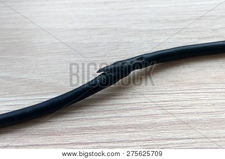 Damaged Black Electric Cord On Wooden Table Or Floor Background. Dangerous Broken Power Electrical C
