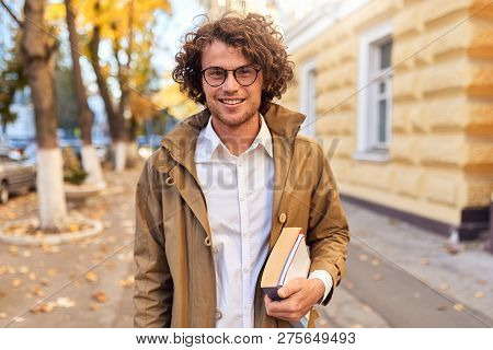 Portrait Of Handsome Young Man With Books Outdoors. College Male Student Carrying Books In College C