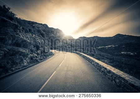 Black & White Image Looking Towards The Sun As It Sets On A Winding Road In The Mountains Of The Bal