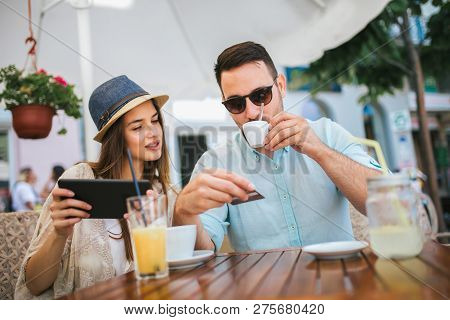 Happy Young Couple Shopping Online While Sitting In A Cafe.