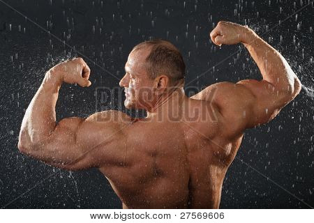 Undressed bodybuilder ยืนในฝนกลับไปยังกล้อง และแสดงกล้ามเนื้อ