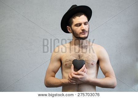 Young Naked Man, With Black Stone Heart In Hands. With A Black Hat On His Head.