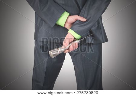 Presenter Is Hodling A Radio Microphone Behind His Back On A Gray Abckground.