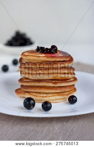 Stack Of American Pancakes With Blackcurrant Jam And Fresh Blackcurrant Are Lying On A White Plate.