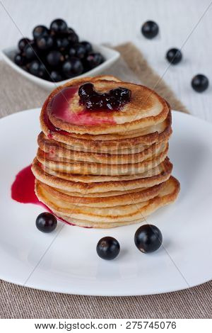 Stack Of American Pancakes With Blackcurrant Jam. Fresh Blackcurrant Are Lying On A White Plate.