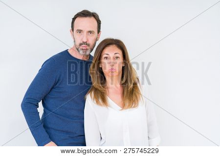 Beautiful middle age couple in love over isolated background puffing cheeks with funny face. Mouth inflated with air, crazy expression.