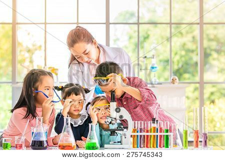 Science Teacher Teach Asian Students In Laboratory Room, Boy  Look Through Microscope, Colorful Test
